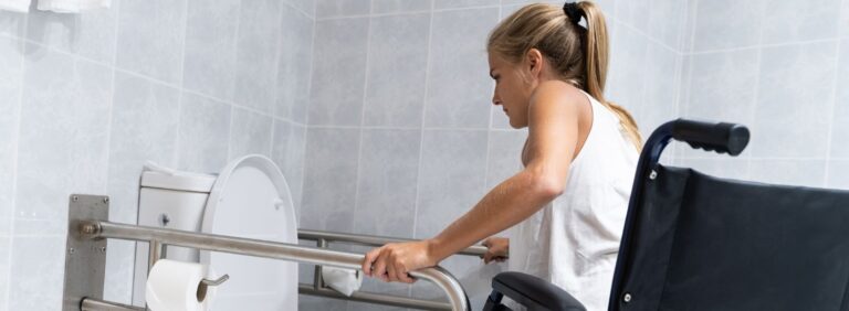 banheiro acessível: mulher em cadeiras de rodas utilizando barras de apoio para sentar em vaso sanitário
