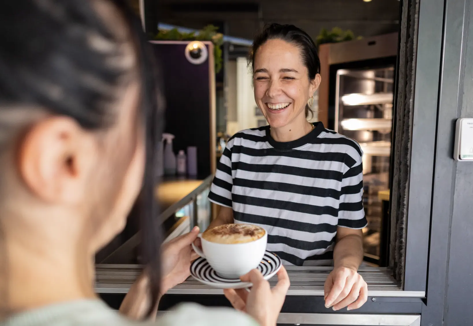 Barista entrega cappuccino a cliente com um sorriso no rosto