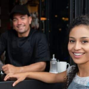 alíquota simples nacional: homem de uniforme atrás do bar e mulher de avental conversando