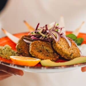 almoço vegano: braços de homem com avental segurando um prato de comida vegana decorado dentro de estabelecimento