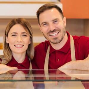 anúncios patrocinados: casal de homem e mulher empreendedores usando uniforme e avental sorrindo atrás do balcão