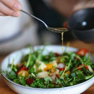 azeite trufado: mão de pessoa branca despejando azeite em tigela de salada com verduras com uma colher