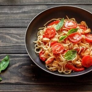 Italian pasta with chicken, tomatoes, red pepper,basil in a pan on a wooden table
