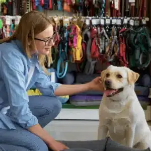 Mulher e criança em um pet shop fazendo carinho em um cachorro de porte grande, branco e com toques amarelados e com a língua para fora