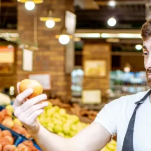Funcionário de supermercado analisa a qualidade de uma fruta