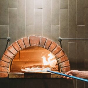 cozinha artesanal: pessoa tirando pizza do forno à lenha