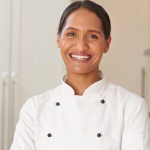 dolmã: mulher negra cozinheira dentro de cozinha utilizando o uniforme branco típico de cozinheiros