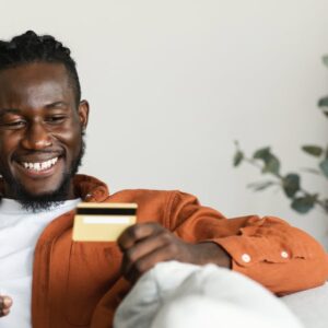 Fast online shopping concept. Positive african american man making financial transaction with credit card and phone