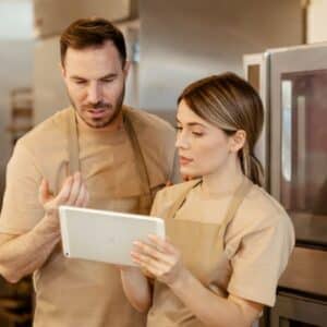 ficha técnica de alimentos: casal de atendentes de uniforme e avental conversando sobre uma ficha técnica