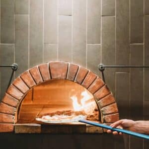 forno de pizza a lenha: pizzaiolo usando uniforme colocando pizza dentro de forno a lenha