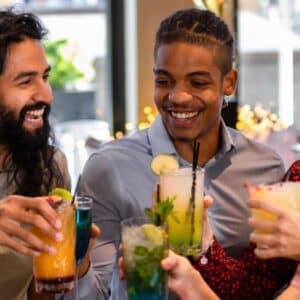 gastrobar: mesa de estabelecimento com seis pessoas diversas em gênero e etnia brindando com drinks na mão enquanto celebram