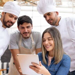 mapa conceitual: empreendedora sentada mostrando tablet para funcionários de avental e cozinheiros de uniforme em pé