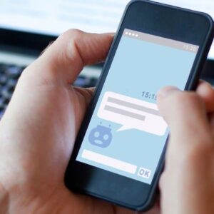 mensagem automática whatsapp: mãos de pessoa branca utilizando o celular para mandar mensagem na frente de um notebook aberto