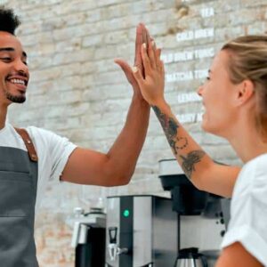 motivação no trabalho: homem e mulher baristas utilizando avental cinza dentro de cafeteria batendo as palmas em comemoração