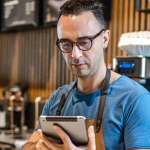 otimização de recursos: homem empreendedor na sua cafeteria utilizando tablet.