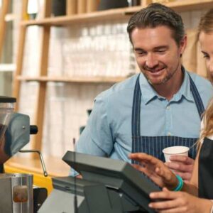 precificação inteligente: homem e mulher com avental atrás do balcão de cafeteria utilizando máquina de pedidos