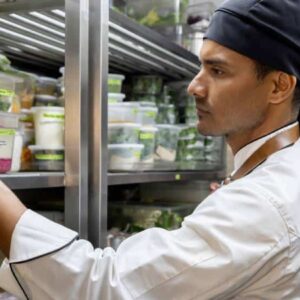 rede de suprimentos: homem assistente de cozinha uniformizado e com avental pegando um ingrediente de prateleira metálica