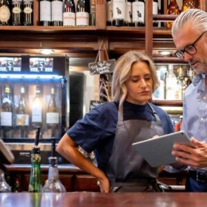 scrum master: homem empreendedor mostrando para mulher atendente informações no tablet. Os dois em pé atrás do balcão.