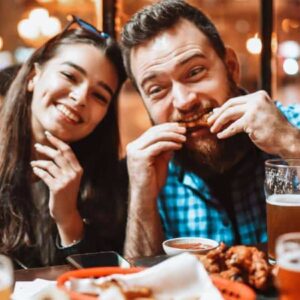 steakhouse: homem e mulher brancos sentados em mesa de restaurante junto com amigos diversos comendo costelas de porco e bebendo cerveja