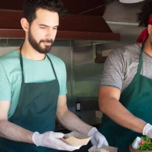 takt time: trio de atendentes de food truck usando avental e luvas enquanto preparam as comidas.