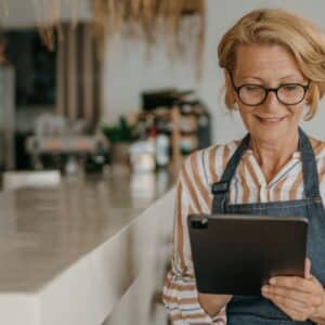 web3: senhora empreendedora usando avental e utilizando um tablet dentro do seu estabelecimento